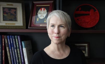 woman with short hair looks off camera, there is a bookshelf and framed images behind her